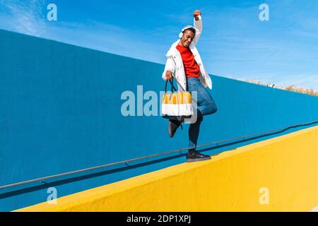 Giovane uomo con borsa, dancing spensierata su una parete di colore giallo Foto Stock