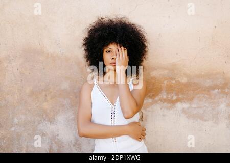 Ritratto di donna afroamericana con i capelli afro con le mani sul viso di fronte al vecchio muro urbano di Granada, Spagna Foto Stock