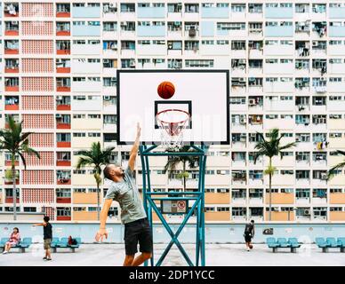 Cina, Hong Kong Kowloon, uomo giocare a basket, alloggiamento pubblico in background Foto Stock