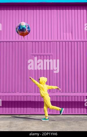 Bambini vestiti in giallo in piedi di fronte al garage viola porta che tiene palloncino Foto Stock
