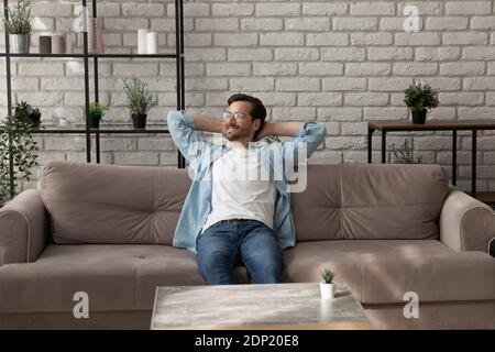 Uomo tranquillo e millenario che si rilassa su un comodo divano dopo aver finito il lavoro Foto Stock