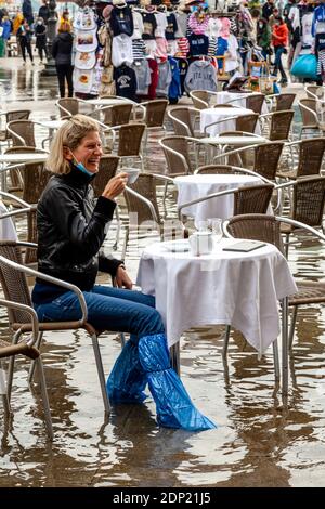 Una donna che beve il tè in un caffè in Piazza San Marco durante l'acqua alta (alta marea), Venezia. Foto Stock