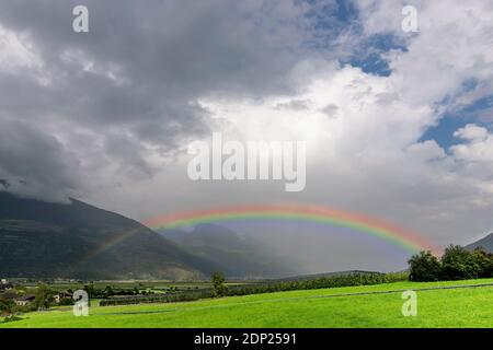 Un grande arcobaleno emerge dalle nubi su un campo di mele piantato in Val Venosta, Prato allo Stelvio, Italia Foto Stock