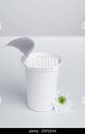 Una tazza generica di yogurt bianco, di plastica, su sfondo bianco, con fiore bianco Foto Stock