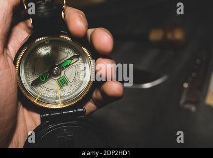 bussola militare in mano. Bushcrafters tenendo la bussola in mano sullo sfondo del coltello e selce. Sopravvivenza in condizioni estreme. Foto Stock