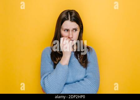 Preoccupata giovane donna ripiegata le mani vicino alla bocca, unghie gnawing, la donna si sente incerta, stressata. Confuso bruna ragazza con paura o panico g Foto Stock