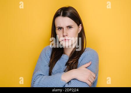 Donna giovane depressa e infelice che guarda la macchina fotografica con un'espressione triste e cupa, ragazza millenaria che si sente insultata o offesa, indossa maglione Foto Stock