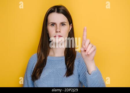 Ritratto di giovane donna brunetta che avverte con un gesto ammonitore delle dita, dicendo di no, dando consigli per evitare il pericolo, vestito in pullover blu Foto Stock