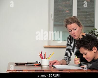 ragazzo imparando a casa con madre e bambino seduto a. una foto di scorta di tabella Foto Stock