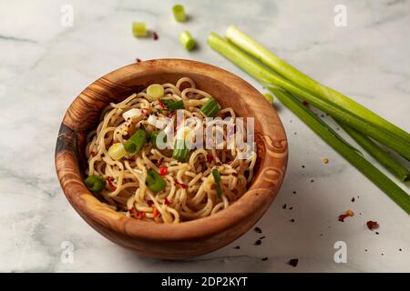 primo piano immagine di una ciotola di legno piena di spaghetti di ramen cotti conditi con erbe e spezie, nonché pezzi di cipolla tritata. Molla sinistra Foto Stock