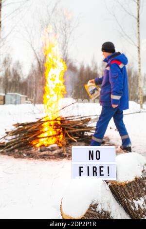 Un uomo in un uniforme blu versa la benzina da un canister nel fuoco. Il concetto di protezione della natura, protezione dagli incendi boschivi, ecologia. Foto Stock