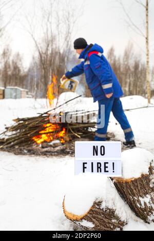 Un uomo in un uniforme blu versa la benzina da un canister nel fuoco. Il concetto di protezione della natura, protezione dagli incendi boschivi, ecologia. Foto Stock