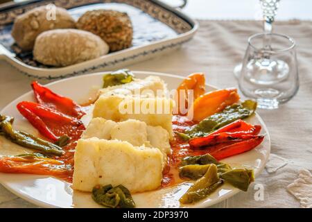 Fette di pesce di merluzzo caldo fritto con fette di peperoni dolci sul piatto bianco. Un piatto con ciambelle sul tavolo servito. Foto Stock