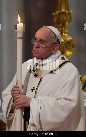 Papa Francesco tiene una candela quando arriva a guidare la messa della veglia pasquale nella basilica di San Pietro in Vaticano il 4 aprile 2015. Papa Francesco ha presieduto la solenne Veglia pasquale sabato sera, in mezzo alla crescente sollecitudine del Vaticano per i martiri cristiani di oggi, le cui morti hanno dominato questo periodo pasquale. Francesco ha camminato nell'oscurità verso la basilica di San Pietro, completamente silenziosa, all'inizio della veglia Messa, che precede la gioiosa celebrazione della domenica di Pasqua, commemorando la risurrezione di Cristo dopo la sua crocifissione. Durante il servizio di notte, 10 persone provenienti dall'Italia, dal Portogallo, da Alba Foto Stock