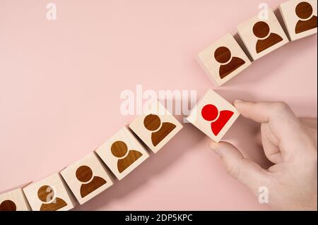 Mano che sceglie un blocco di persona di legno da un insieme. Concetto di scelta dell'occupazione. Risorse umane HR Management assunzioni Employment Concept. Pink backgrou Foto Stock