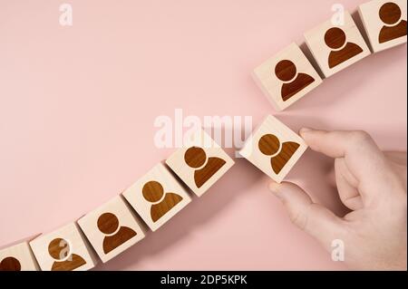 Risorse umane HR Management Assunzione Employment Concept. Mano che sceglie un blocco di persona di legno da un insieme. Sfondo rosa, spazio di copia. Foto Stock