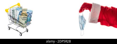Colpo laterale della mano di Babbo Natale che tiene una maschera medica accanto ad un carrello pieno di euro e dollari bollette. Nuovo concetto di shopping normale, nuova realtà. Bann Foto Stock