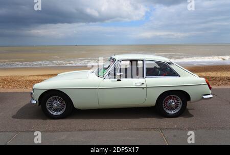 Classica Whie MGB GT Motor Car parcheggiata sul lungomare con spiaggia e mare sullo sfondo. Foto Stock