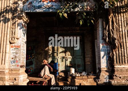 Jamnagar, Gujarat, India - Dicembre 2018: Un anziano indiano che vende il tè sotto le colonne e le pareti sopravsviluppate di un vecchio edificio . Foto Stock