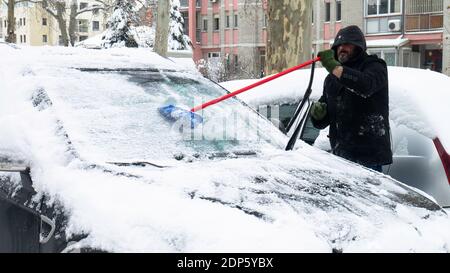 L'uomo libera la neve dal ghiaccio del parabrezza dell'auto. Foto Stock