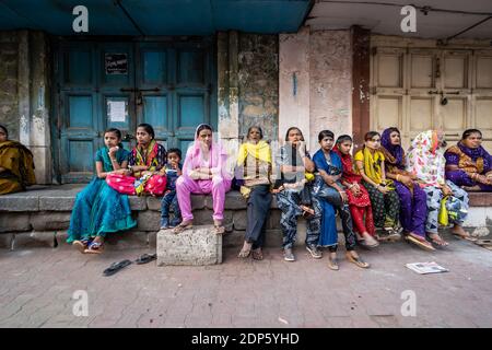 Jamnagar, Gujarat, India - Dicembre 2018: Un grande gruppo di donne indiane che indossano abiti colorati seduti su un portico a bordo strada nelle strade del cit Foto Stock