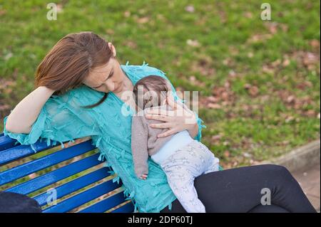 Depressa bella donna su una panchina del parco con il suo bambino in cima. Foto Stock