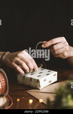 Una femmina che avvolge un regalo di Natale con carta riciclato di abete, burlap e foglie di abete Foto Stock