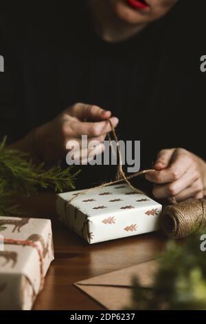 Una femmina che avvolge un regalo di Natale con carta riciclato di abete, burlap e foglie di abete Foto Stock