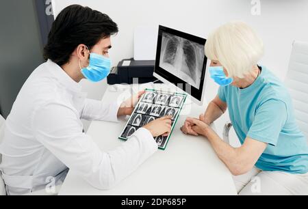 Pulmonologa indossando una maschera protettiva che mostra ad un paziente anziano una scansione TC dei polmoni. Polmonite, coronavirus, malattie polmonari Foto Stock