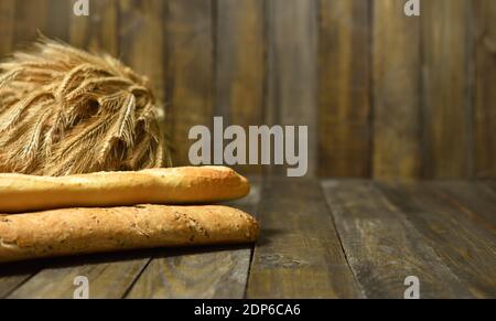 Baguette francese lunga e spighe di grano su sfondo di legno Foto Stock