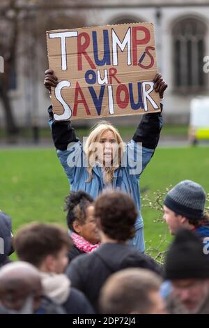 Ritratto di una donna che tiene un cartello "Trump è il nostro Salvatore" sopra la folla durante la protesta contro il vaccino COVID-19, Parliament Square, Londra, 14 dicembre Foto Stock