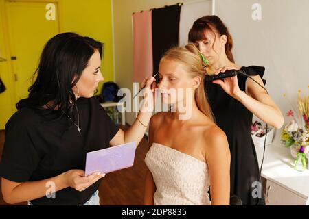 Backstage preparare giovane bella modellatrice stylist parrucchiere e trucco artista lavoro su modello in salone di bellezza Foto Stock