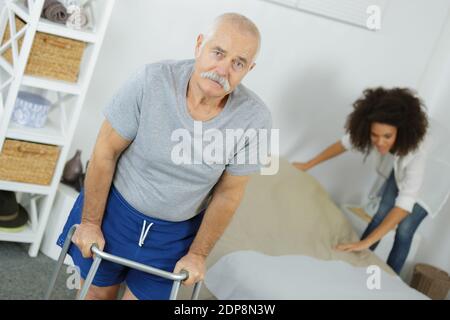 uomo anziano che cammina con telaio carer che fa letto in background Foto Stock