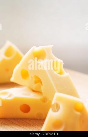 Pezzi triangolari di formaggio giallo svizzero con fori su piastra di legno. Formaggio di mucca olandese Maasdam Foto Stock