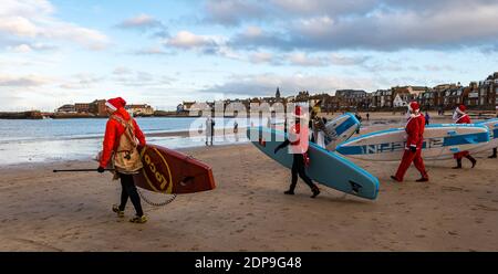 North Berwick, East Lothian, Scozia, Regno Unito, 19 dicembre 2020. Paddle Boarding Santas per beneficenza: Un'iniziativa della comunità locale di North Berwick News e viste chiamato 'Christmas Cheer' raccoglie oltre £5,000 fondi per le famiglie in difficoltà, i paddle boarders vestiti in costumi di Santa portare le loro tavole da paddle attraverso la spiaggia Foto Stock