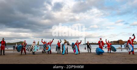 North Berwick, East Lothian, Scozia, Regno Unito, 19 dicembre 2020. Paddle imbarco Santas per la carità: Un'iniziativa locale della comunità da North Berwick News e opinioni chiamato 'Christmas Cheer' raccoglie oltre £5,000 fondi per le famiglie in bisogno. I paddle boarders vestiti in costumi di Santa posa per una foto sulla spiaggia Foto Stock