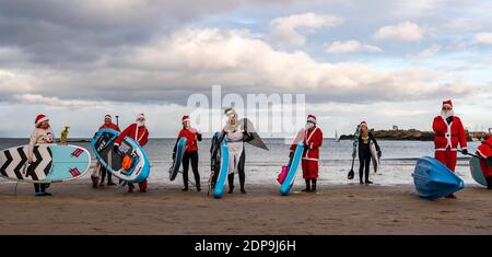 North Berwick, East Lothian, Scozia, Regno Unito, 19 dicembre 2020. Paddle imbarco Santas per la carità: Un'iniziativa locale della comunità da North Berwick News e opinioni chiamato 'Christmas Cheer' raccoglie oltre £5,000 fondi per le famiglie in bisogno. I paddle boarders vestiti in costumi di Santa posa per una foto sulla spiaggia Foto Stock