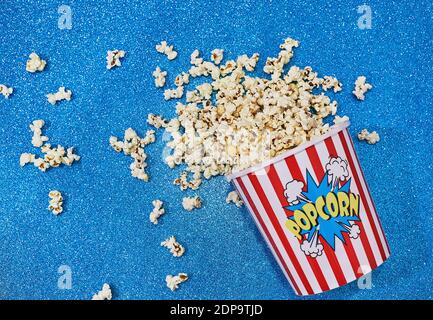 Una disposizione piatta di una tazza di carta grande riempita con popcorn su una superficie blu brillante Foto Stock