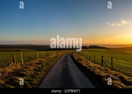 Guardando lungo una strada di campagna a Firle Beacon, con un cielo tramonto davanti Foto Stock
