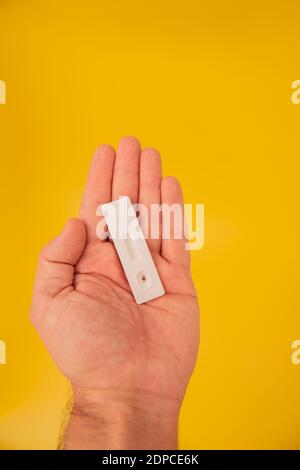 Mano maschio che mostra il test dell'antigene con risultato negativo su sfondo giallo. Foto Stock