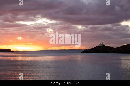 Alba, tramonto sulla Grecia, isola di Kea Tzia. Faro bianco su promontorio roccioso, raggi solari dorati attraverso colori cielo nuvoloso increspato mare scintillante acqua indietro Foto Stock