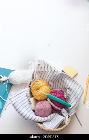 Vista dall'alto di alcune colorate palle di filato all'interno di un petto di vimini. Un ago da cucire verde e un misuratore da cucire sono nella parte superiore. Foto Stock