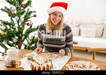 Felice bella donna nel cappello di santa che celebra il Natale con la torta e pino a casa Foto Stock