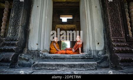 Siem Reap, Cambogia - Dicembre 2015: Bambini monaco seduti da una porta di pietra nelle rovine di Angkor Wat. Angkor Wat è il più grande monumento religioso del WO Foto Stock