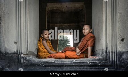 Siem Reap, Cambogia - Dicembre 2015: Bambini monaco seduti da una porta di pietra nelle rovine di Angkor Wat. Angkor Wat è il più grande monumento religioso del WO Foto Stock