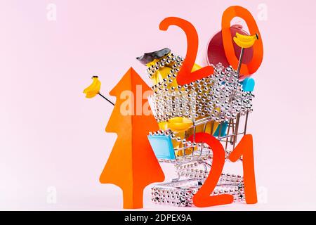 Decorazioni dell'albero di Natale nel carrello della spesa su sfondo rosa. Albero di Natale rosso e l'iscrizione 2021 nel carrello. Vacanze shoppi Foto Stock