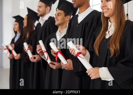 Gruppo di persone multietniche che si trovano di fila e che tengono rotoli di diplomi nelle loro mani. Foto Stock