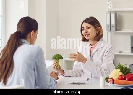 Nutrizionista che tiene broccoli e che dice alla giovane donna circa i benefici di mangiare sano Foto Stock