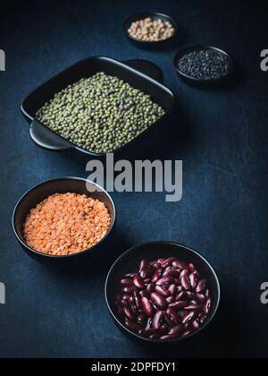 Ciotole nere di vari legumi secchi - fagioli, lenticchie, fagioli mungo e ceci su sfondo blu scuro. Spazio di copia. Buio e moody. Foto Stock