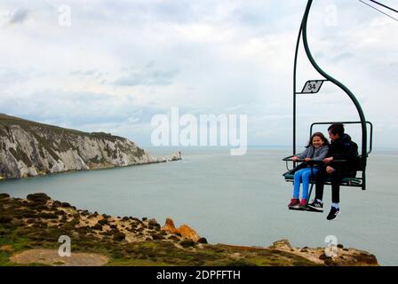 Due bambini che si divertano a fare un giro sulla seggiovia, Alum Bay, Isle of Wight con il faro di Needles in lontananza Foto Stock